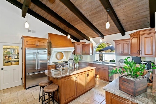 kitchen featuring a center island with sink, stone tile floors, stainless steel appliances, visible vents, and premium range hood