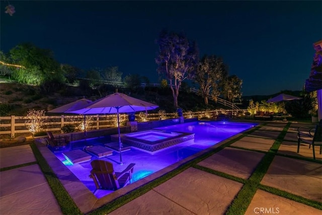 pool at twilight with an infinity pool, an in ground hot tub, a patio, and fence