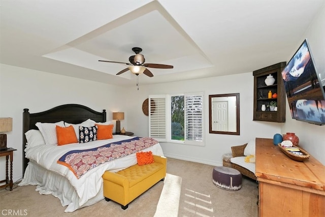 carpeted bedroom featuring a tray ceiling, ceiling fan, and baseboards