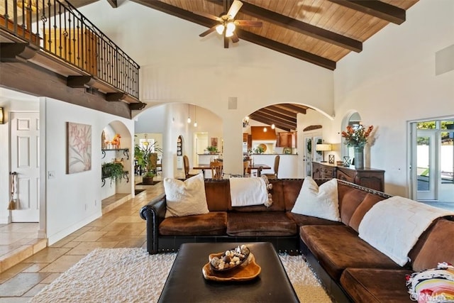 living room featuring high vaulted ceiling, stone tile floors, wood ceiling, baseboards, and beam ceiling