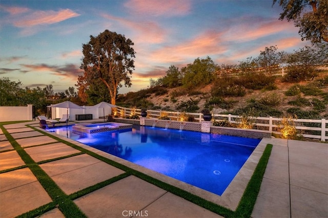 pool at dusk featuring a patio area, a fenced backyard, and a pool with connected hot tub