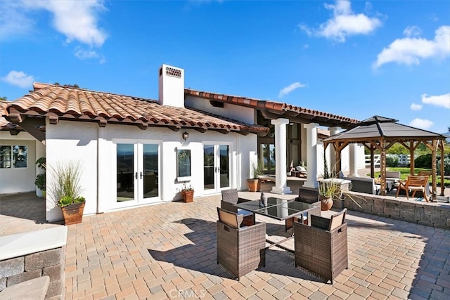 exterior space with french doors, a tile roof, a chimney, a gazebo, and a patio area