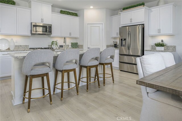 kitchen featuring white cabinets, light wood-style flooring, stainless steel appliances, and an island with sink