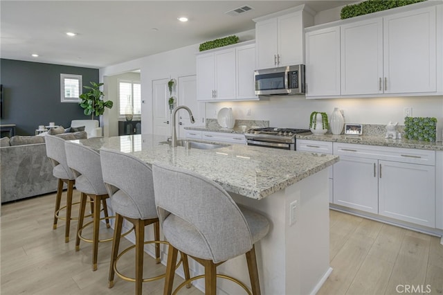 kitchen featuring light wood finished floors, visible vents, open floor plan, stainless steel appliances, and a sink