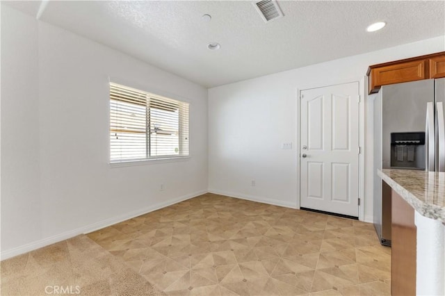 interior space with brown cabinetry, stainless steel refrigerator with ice dispenser, baseboards, and a textured ceiling