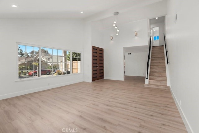 unfurnished living room featuring stairs, light wood finished floors, a high ceiling, and baseboards