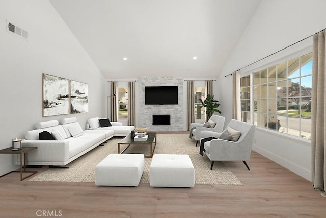 living area featuring high vaulted ceiling, a large fireplace, visible vents, and wood finished floors