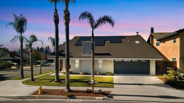 view of front of house featuring a garage, solar panels, driveway, a lawn, and stucco siding