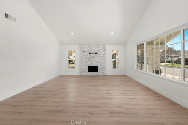 unfurnished living room featuring baseboards, visible vents, light wood-type flooring, a fireplace, and high vaulted ceiling