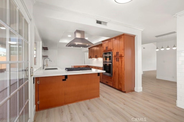 kitchen featuring stainless steel double oven, light wood-style flooring, island range hood, a peninsula, and a sink