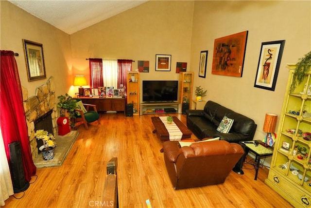 living area featuring lofted ceiling, a stone fireplace, and wood finished floors