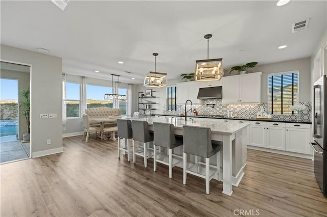 kitchen with visible vents, backsplash, light wood-style floors, white cabinets, and under cabinet range hood