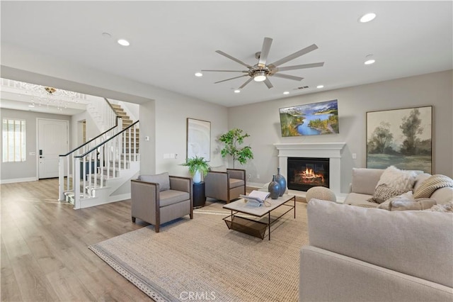 living area with stairs, a glass covered fireplace, wood finished floors, and recessed lighting