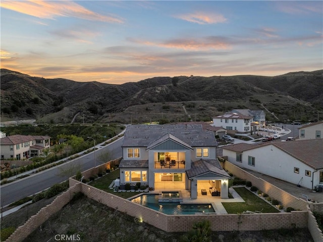 back of property at dusk featuring a fenced in pool, a lawn, a mountain view, a balcony, and a fenced backyard