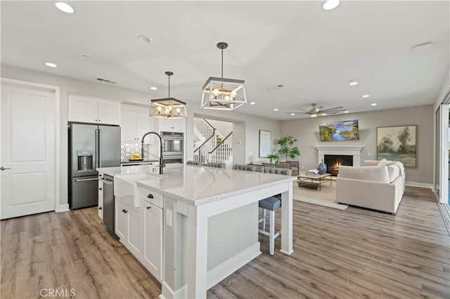 kitchen featuring a warm lit fireplace, appliances with stainless steel finishes, light wood finished floors, and white cabinets