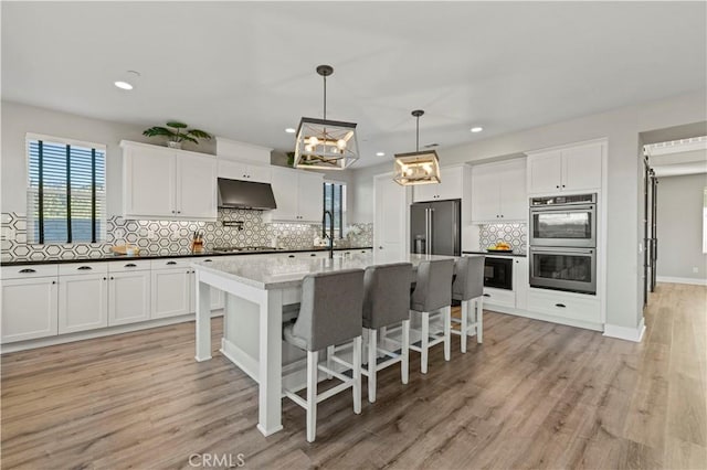 kitchen featuring stainless steel double oven, white cabinets, high quality fridge, and under cabinet range hood