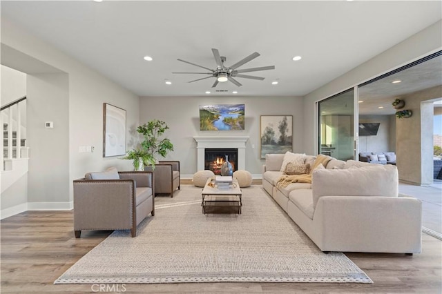 living room featuring light wood-style flooring, recessed lighting, baseboards, stairs, and a glass covered fireplace