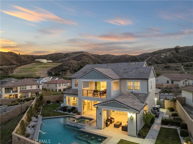 rear view of property with a pool with connected hot tub, a fenced backyard, a mountain view, and a balcony