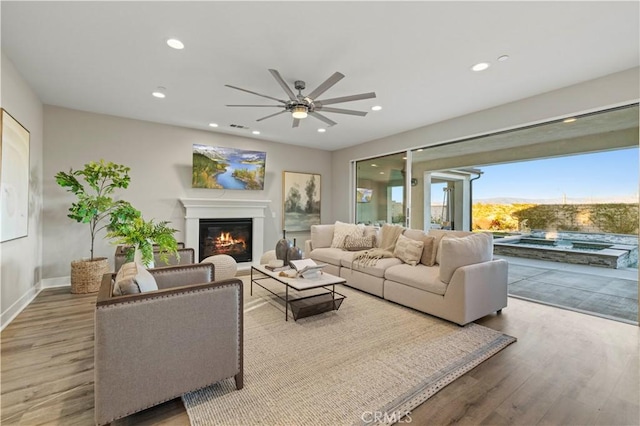 living area featuring recessed lighting, a glass covered fireplace, ceiling fan, wood finished floors, and baseboards