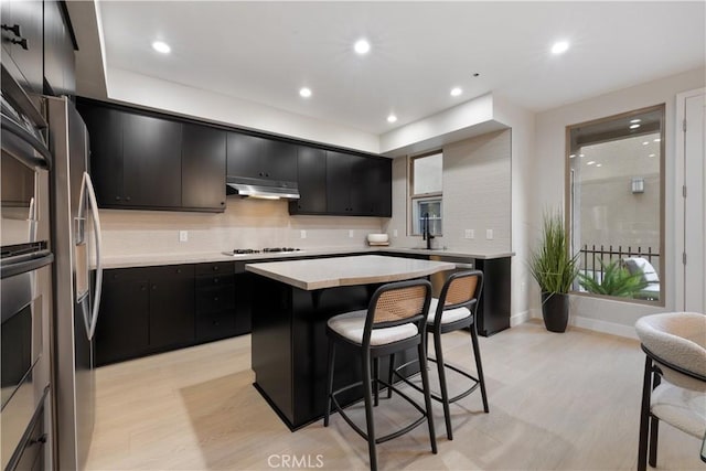 kitchen with a kitchen breakfast bar, light wood-style floors, dark cabinets, and under cabinet range hood