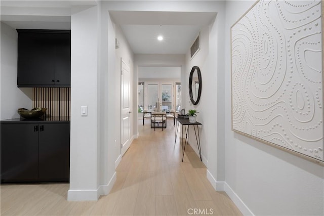 hall with light wood-type flooring, visible vents, and baseboards