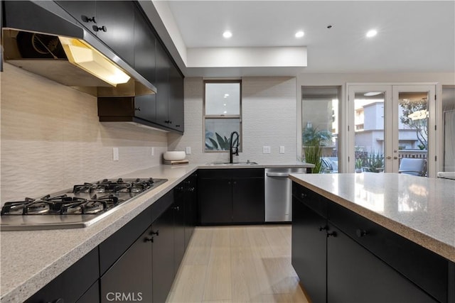 kitchen featuring stainless steel appliances, dark cabinetry, a sink, and under cabinet range hood