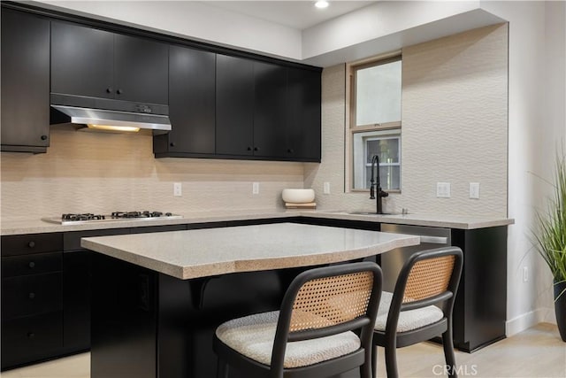 kitchen with a breakfast bar area, stainless steel appliances, dark cabinetry, under cabinet range hood, and a sink