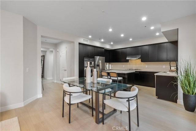 kitchen featuring visible vents, stainless steel appliances, dark cabinetry, under cabinet range hood, and a sink