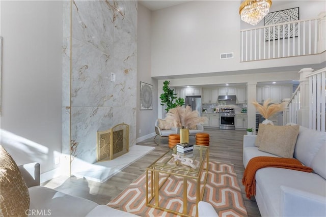 living area with a chandelier, a high ceiling, a fireplace, visible vents, and stairway