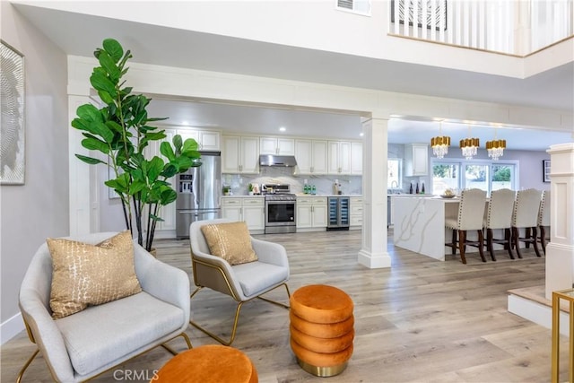 living area with ornate columns, wine cooler, visible vents, and light wood finished floors