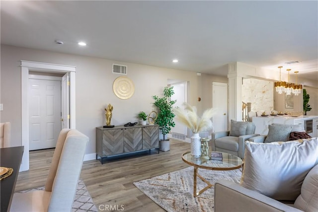 living area with a notable chandelier, recessed lighting, wood finished floors, visible vents, and baseboards