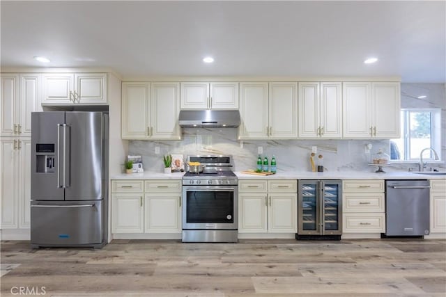 kitchen featuring under cabinet range hood, beverage cooler, a sink, light countertops, and appliances with stainless steel finishes