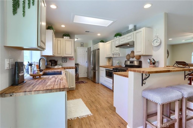 kitchen with butcher block counters, a breakfast bar area, stainless steel appliances, under cabinet range hood, and a sink