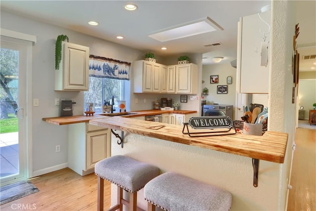 kitchen with recessed lighting, a sink, a kitchen breakfast bar, wooden counters, and light wood finished floors