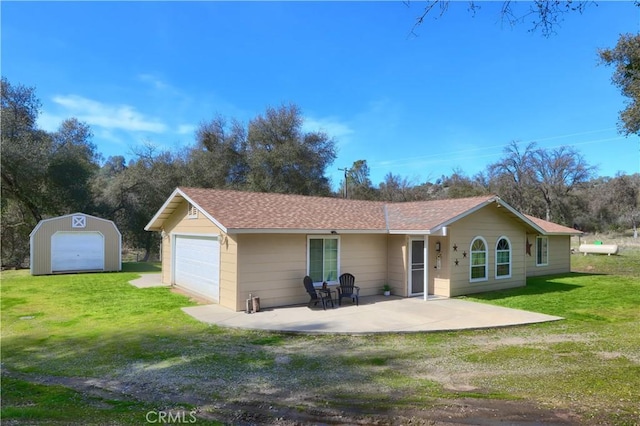 rear view of property featuring a shingled roof, a patio, an outbuilding, a yard, and a shed