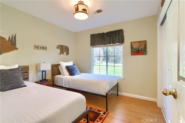 bedroom with light wood-type flooring, baseboards, visible vents, and a closet