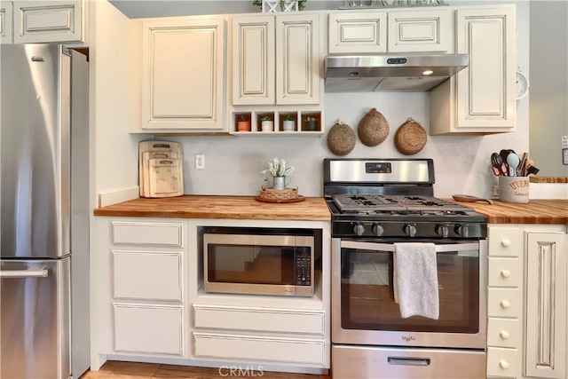 kitchen featuring under cabinet range hood, cream cabinetry, stainless steel appliances, and wooden counters