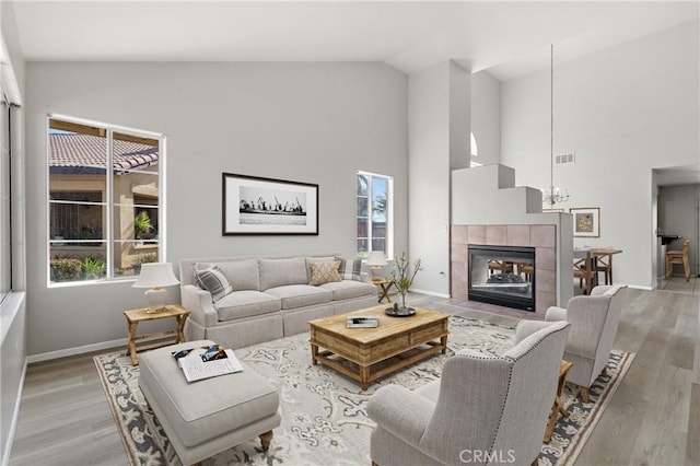 living area with visible vents, baseboards, light wood-type flooring, a tile fireplace, and high vaulted ceiling