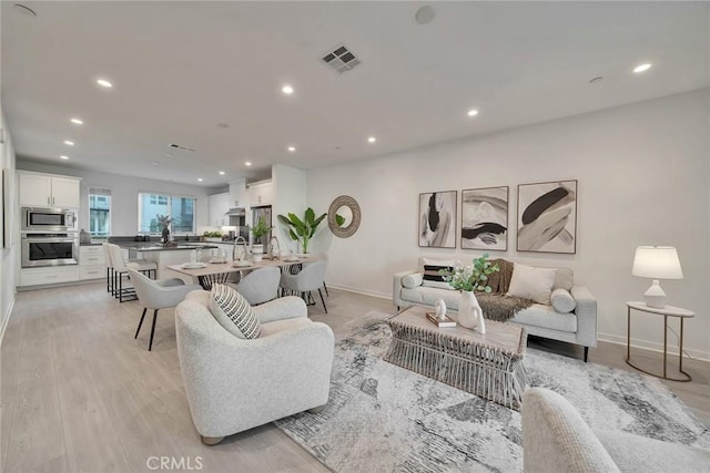 living room featuring light wood-style floors, baseboards, visible vents, and recessed lighting