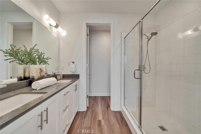 full bathroom featuring double vanity, a sink, a shower stall, wood finished floors, and baseboards