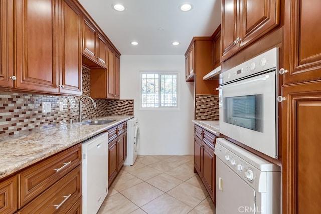 kitchen featuring white appliances, washer / clothes dryer, brown cabinets, and a sink