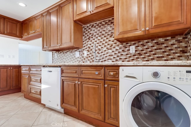 kitchen with light tile patterned floors, washer / clothes dryer, a sink, brown cabinets, and tasteful backsplash