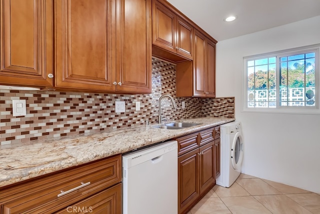 kitchen with light tile patterned floors, white dishwasher, a sink, brown cabinets, and washer / clothes dryer