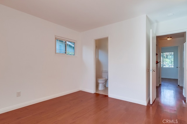 unfurnished bedroom with connected bathroom, baseboards, and wood finished floors