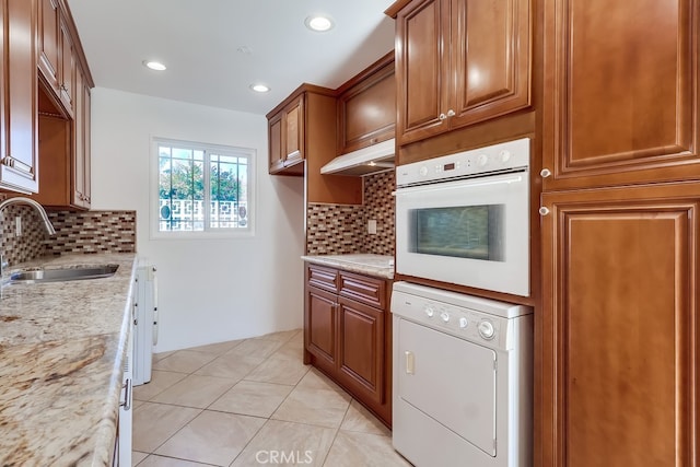 kitchen with washer / clothes dryer, brown cabinetry, a sink, oven, and under cabinet range hood