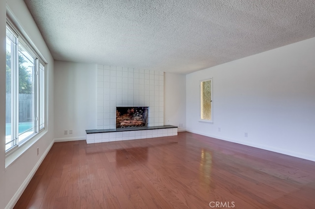 unfurnished living room featuring dark wood-type flooring, a tile fireplace, a textured ceiling, and baseboards