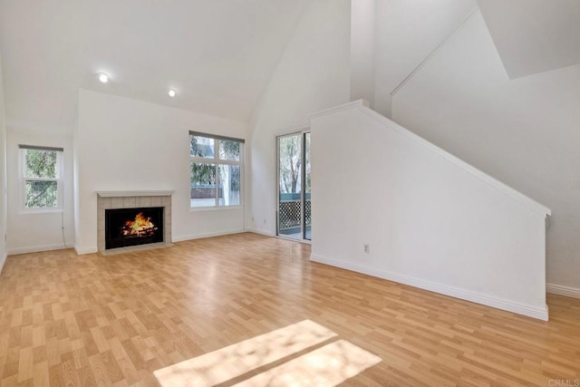 unfurnished living room featuring stairs, a fireplace, high vaulted ceiling, and a wealth of natural light