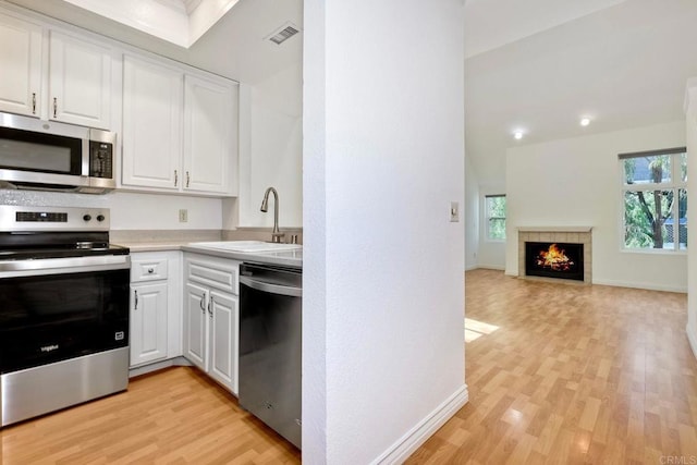 kitchen featuring visible vents, appliances with stainless steel finishes, a fireplace, white cabinetry, and a sink