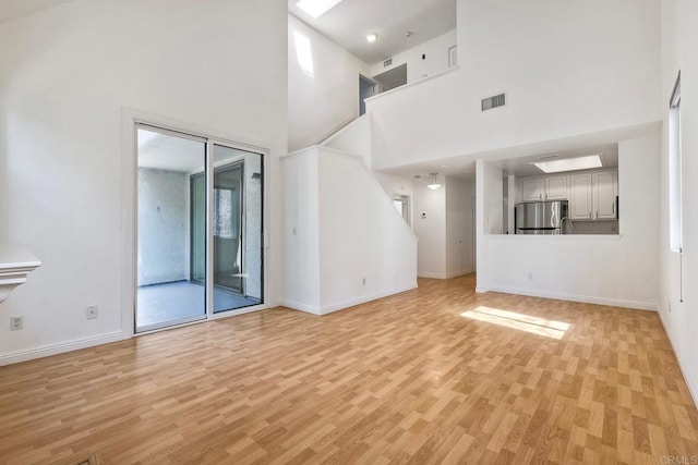 unfurnished living room with light wood-style flooring, a high ceiling, visible vents, and baseboards