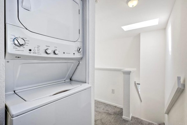 laundry room featuring a skylight, light colored carpet, stacked washing maching and dryer, laundry area, and baseboards